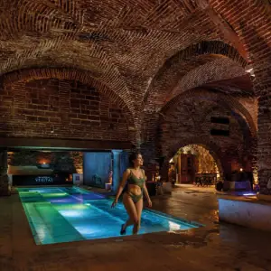 Ambiente interior com arcos e pormenores clássicos no Spa In Acqua Veritas, evocando o encanto intemporal dos antigos banhos romanos.
